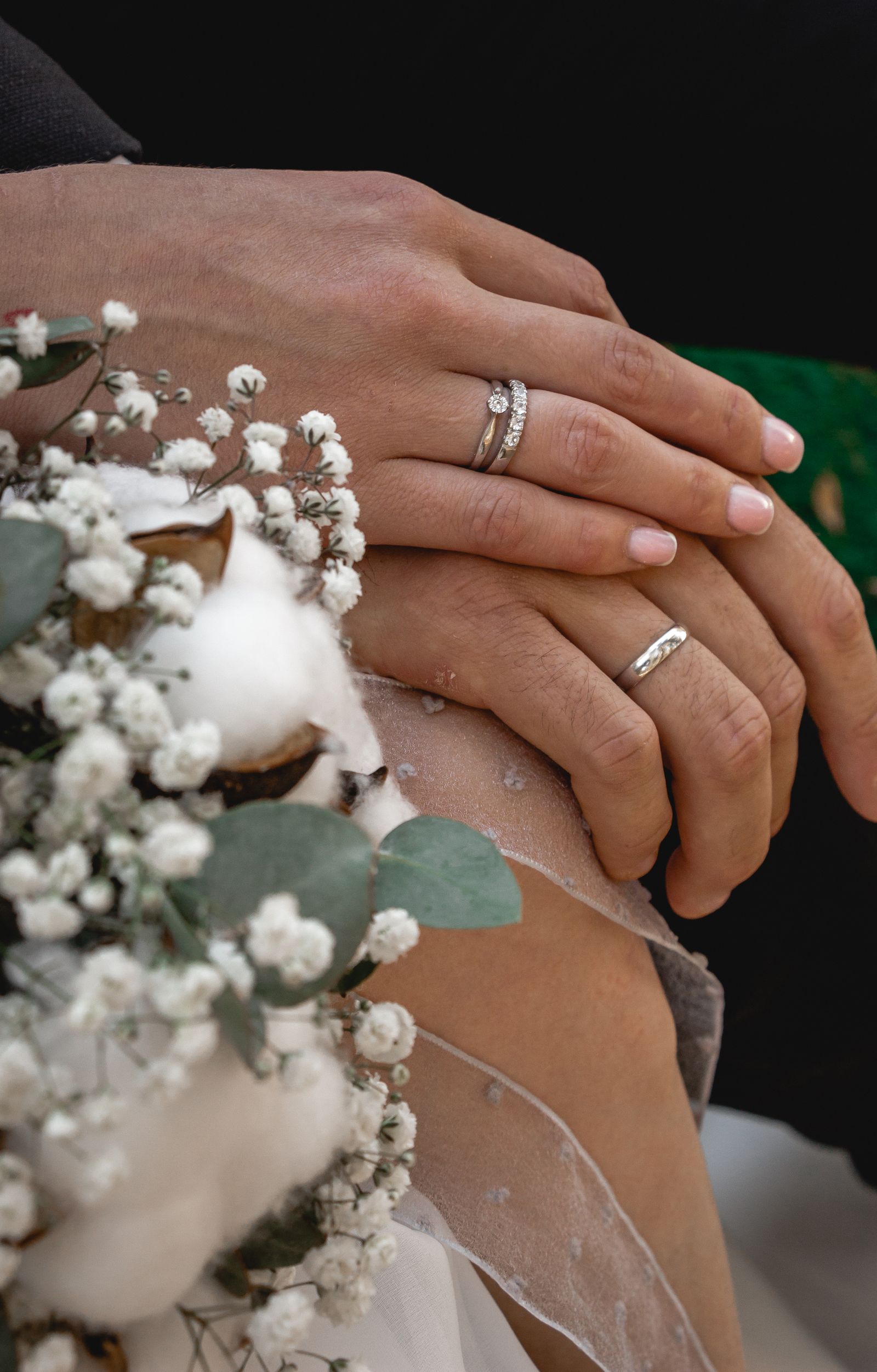 Bride and groom's hands with wedding rings resting on a bouquet of cotton and baby's breath